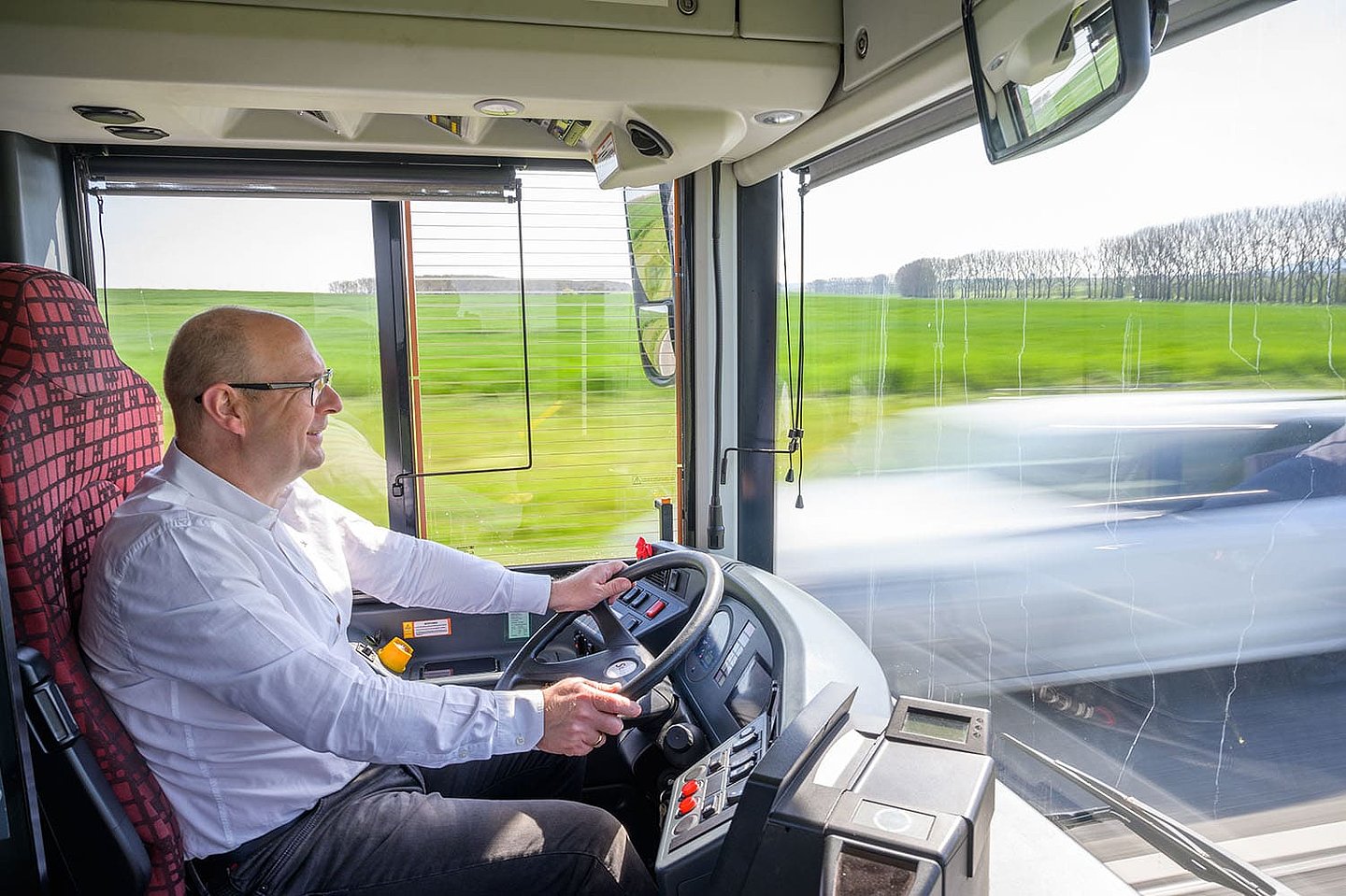 ein Busfahrer schaut lächelnd aus seinem Bus heraus auf die Straße
