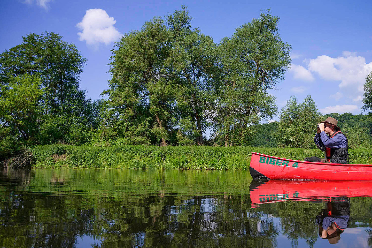 ein durch ein Fernglas schauender Mann fährt mit einem Kajak über einen Fluss