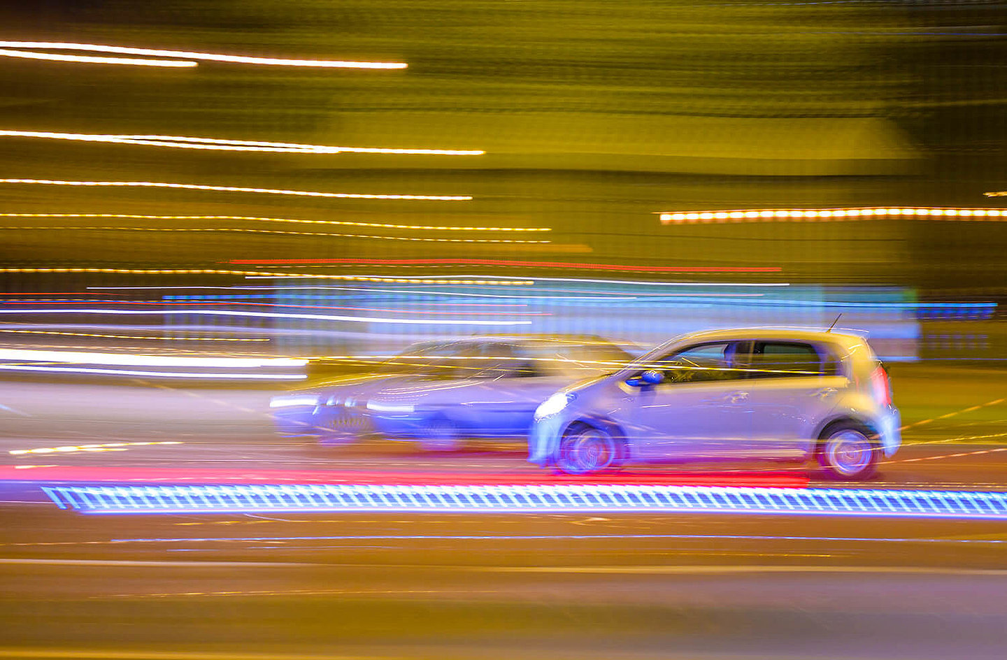 Zwei bei Nacht vorbeifahrende Autos, welche durch das Licht verschwommen wirken