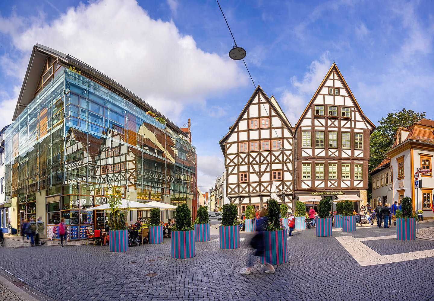 ein modernes und zwei alte Fachwerkhäuser an der Krämerbrücke, vor denen bepflanzte Blumenkübel stehen