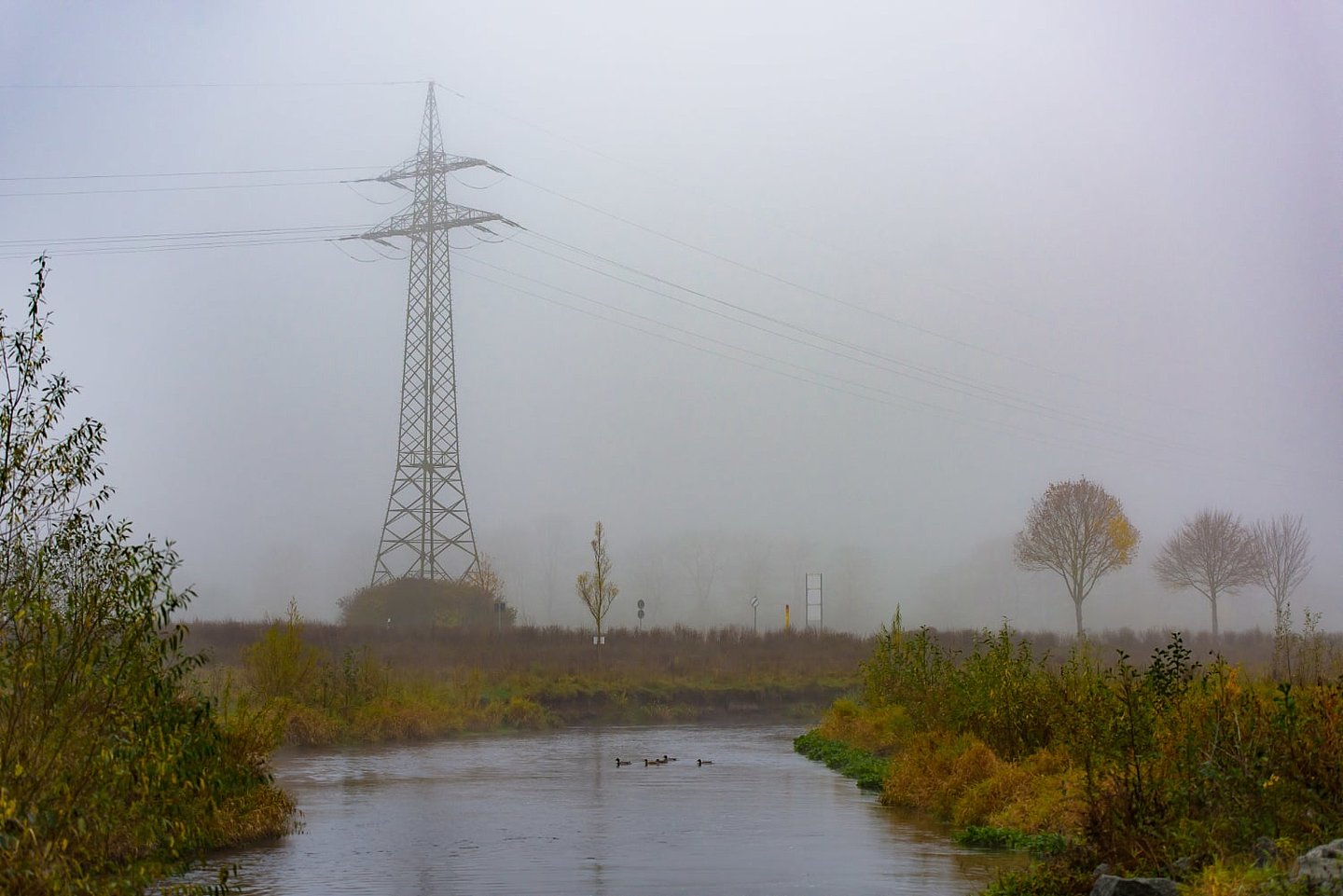 Fluss und Strommast im Nebel