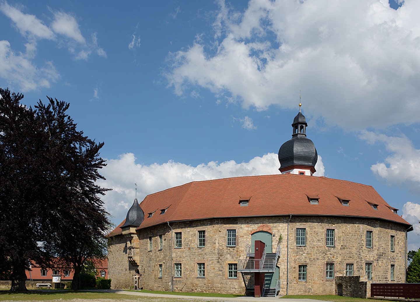 Aufnahme des Schloss Blankenhains in der Totale. Am linken Bildrand steht ein großer Baum.