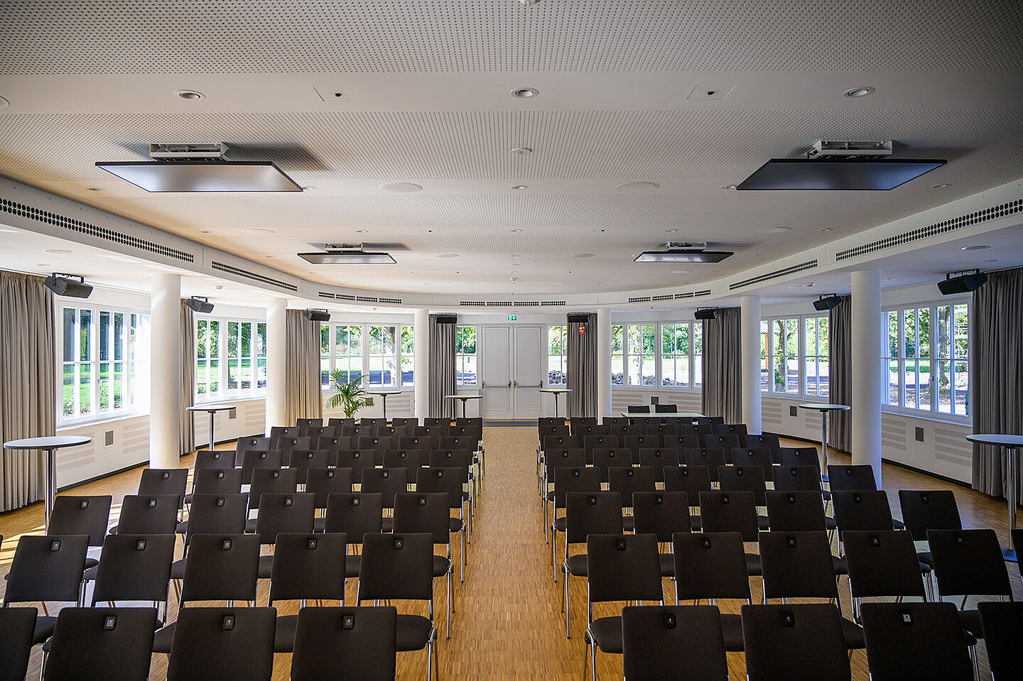 Der große Helle Festsaal mit vielen aneinander gereiten Stühlen.