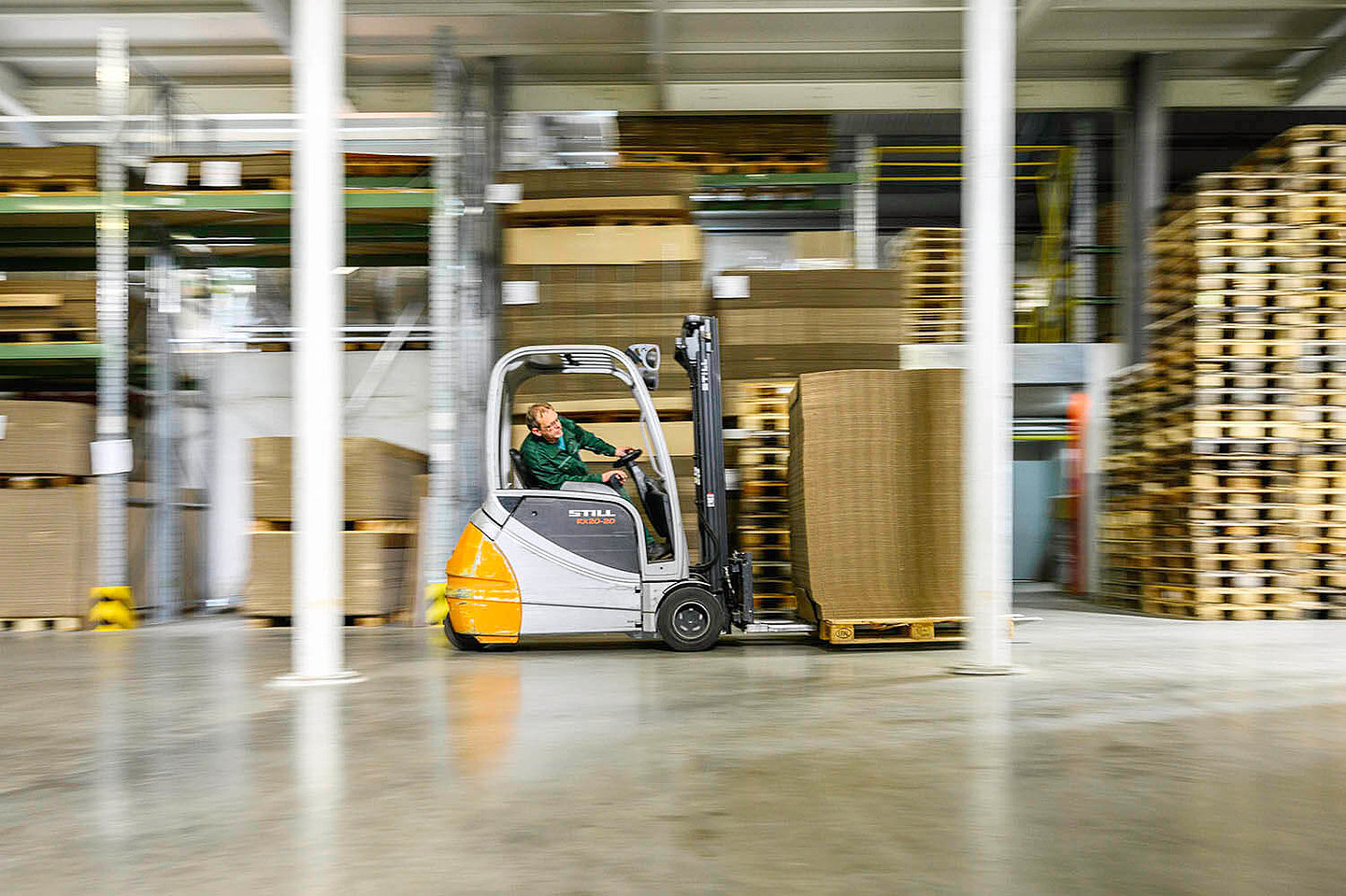 ein Gabelstaplerfahrer Fährt Verpackungen durch eine Lagerhalle