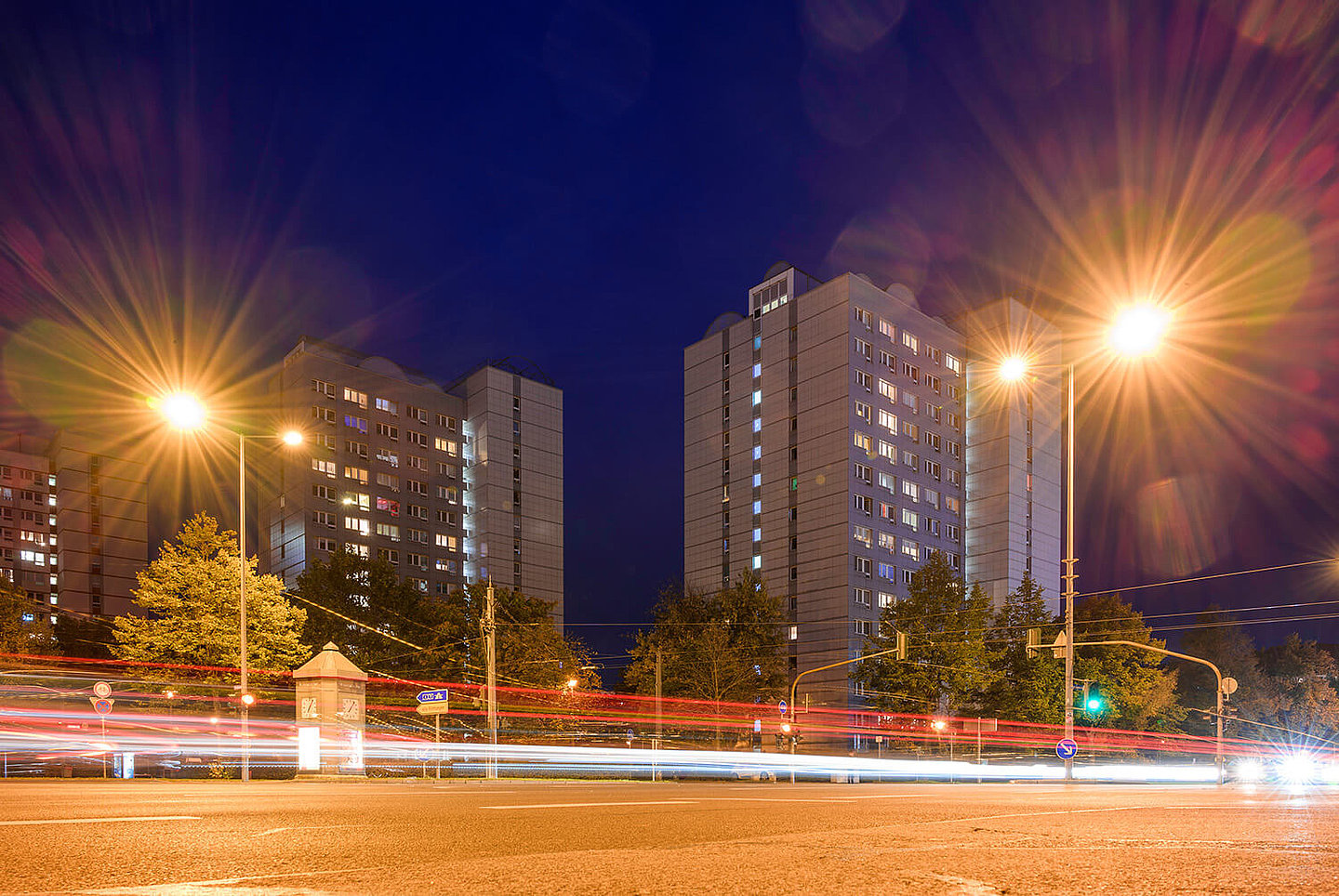 Eine viel befahrene Straße bei Nacht, hinter welcher Wohnblocks stehen