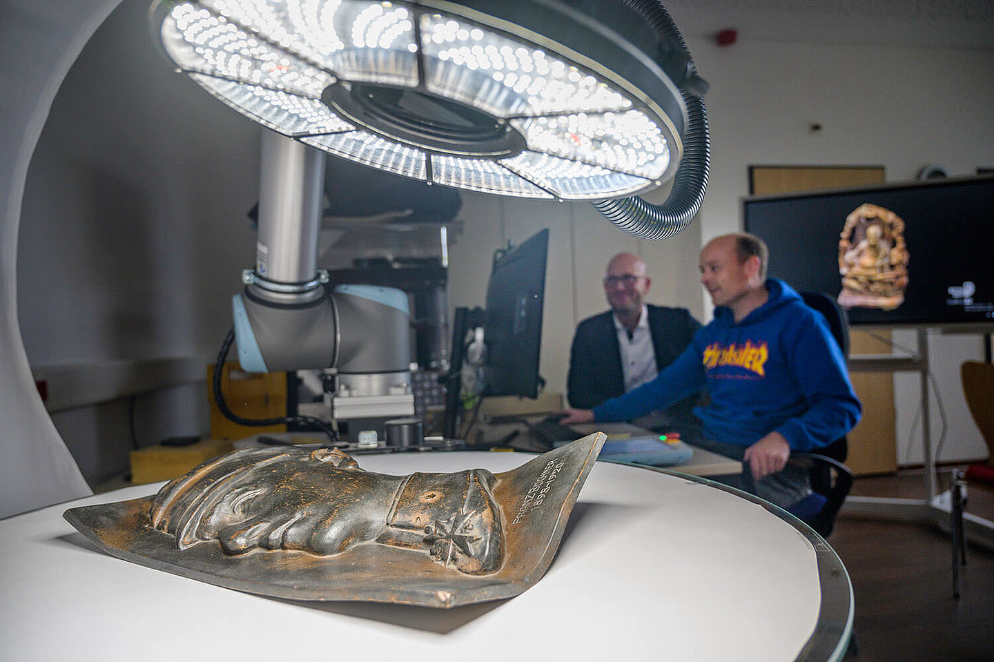 zwei Männer sehen sich über ihren Monitor eine hell beleuchtete Bronze-Skulptur an