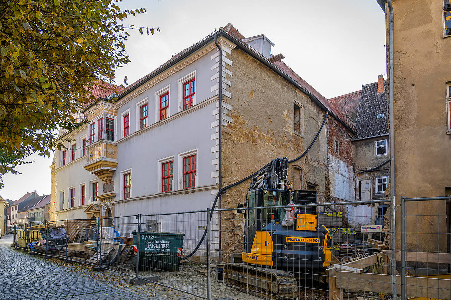 Die Baustelle am Rathaus. Ein Bagger und mehrere Schuttcontainer sind mit einem Bauzaun umschlossen.