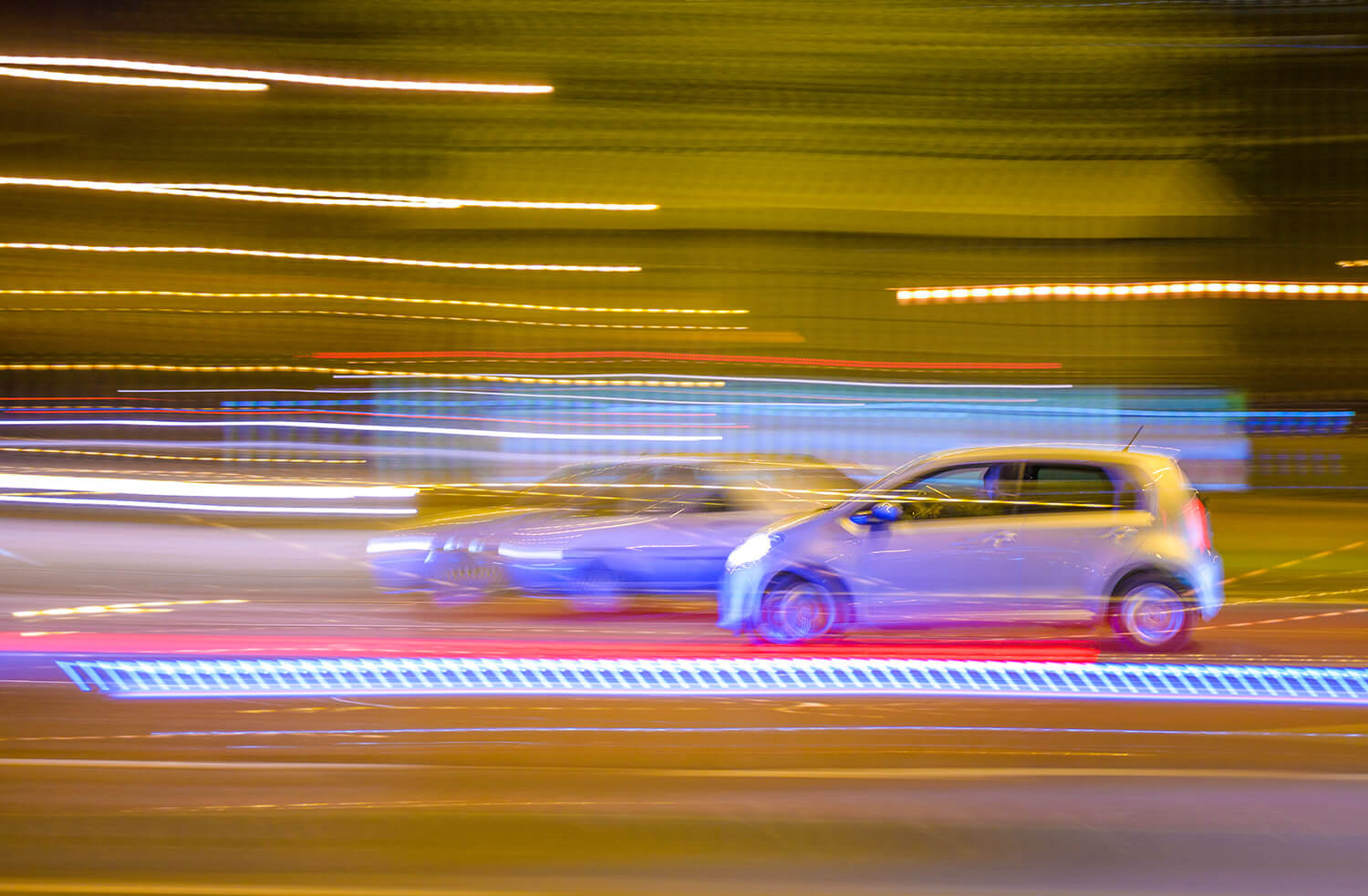 Zwei bei Nacht vorbeifahrende Autos, welche durch das Licht verschwommen wirken